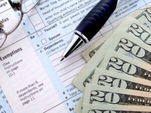 Close up of tax forms, glasses, money, and a pen.