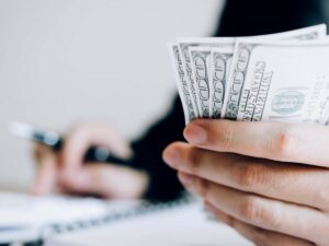 Close up of hundred dollar bills held in someone’s hand while they calculate costs.
